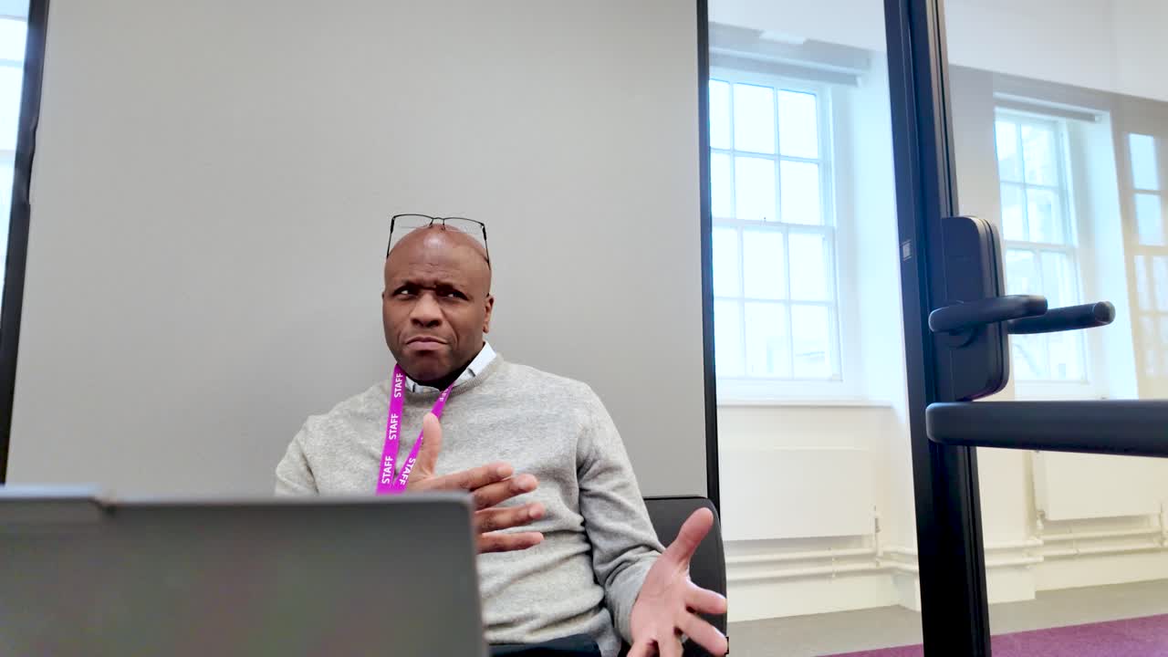 Black Businessman gesturing while talking in a modern soundproof office pod with a laptop on the desk