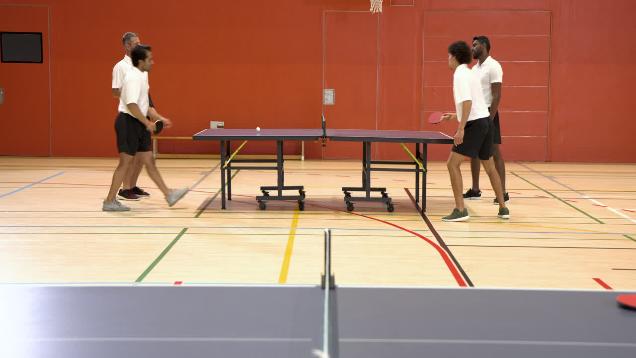 Playing table tennis, four men enjoying doubles match in gymnasium
