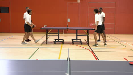 playing table tennis, four men enjoying doubles match in gymnasium