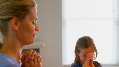 Side-view-of-young-Caucasian-mother-and-daughter-praying-together-at-dining-table-in-a-comfortable-h