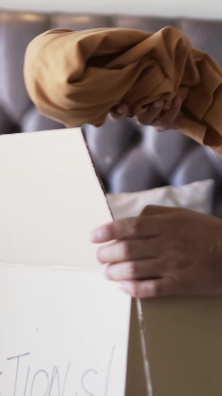 Video verticale: Apertura di una scatola, mani maschili che tirano e posizionano una camicia color senape in una scatola per donazioni a casa
