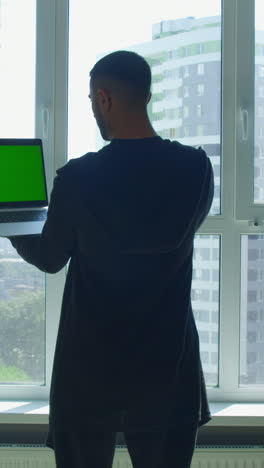 hombre mirando por la ventana con una computadora portátil