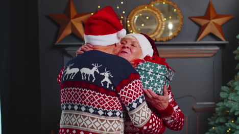 Senior-family-couple-grandmother-presenting-Christmas-gift-box-to-amazed-grandfather-at-home-room