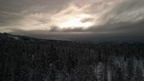 Drohne,-Die-über-Eine-Winterlandschaft-Fliegt,-Wobei-Die-Sonne-In-Der-Ferne-Durch-Die-Wolken-Späht