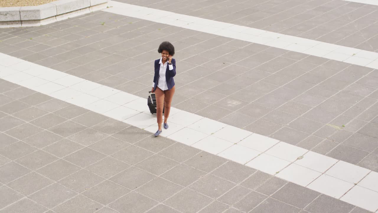 African american businesswoman talking on smartphone and walking with luggage