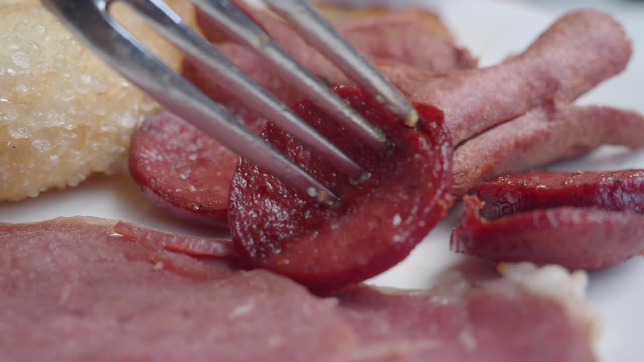 Primo piano di una forchetta che prende del salame da un piatto da colazione