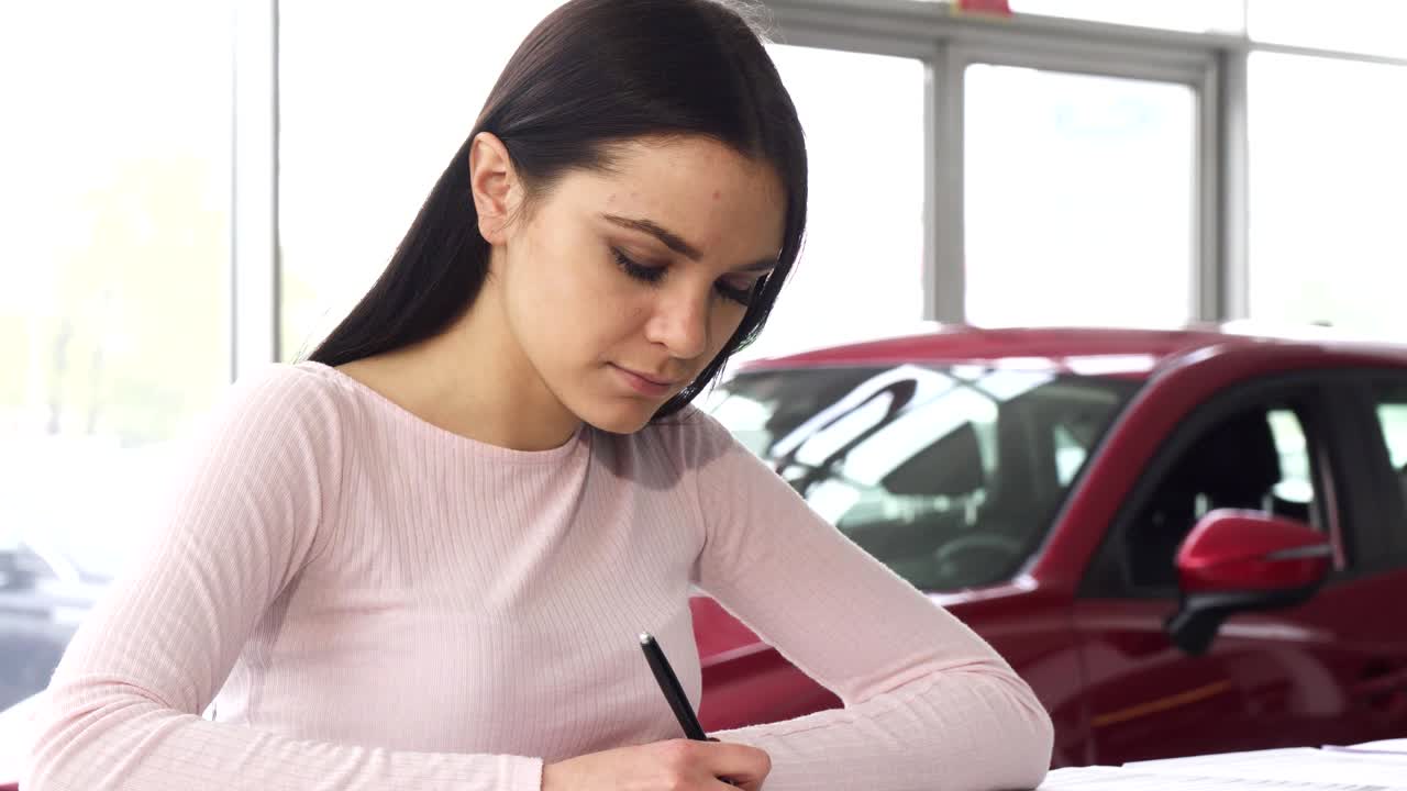 hermosa mujer joven firmando papeles en la sala de exposición del concesionario