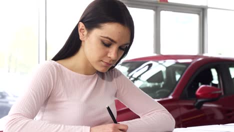 beautiful young woman signing papers at the dealership showroom