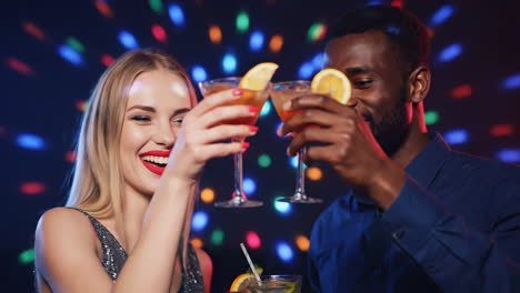 happy multiethnic couple cheering with cocktails at a disco party