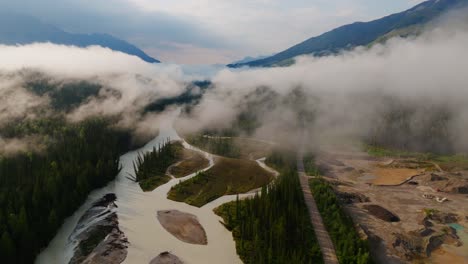 Drone-shot-emerging-through-a-layer-of-clouds-to-reveal-the-Kicking-Horse-River-and-looking-toward-mountains-and-into-Yoho-National-Park