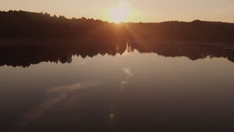 sobrevolando el lago tranquilo con un hombre remando en un bote sobre las aguas tranquilas durante una puesta de sol naranja ardiente en polonia