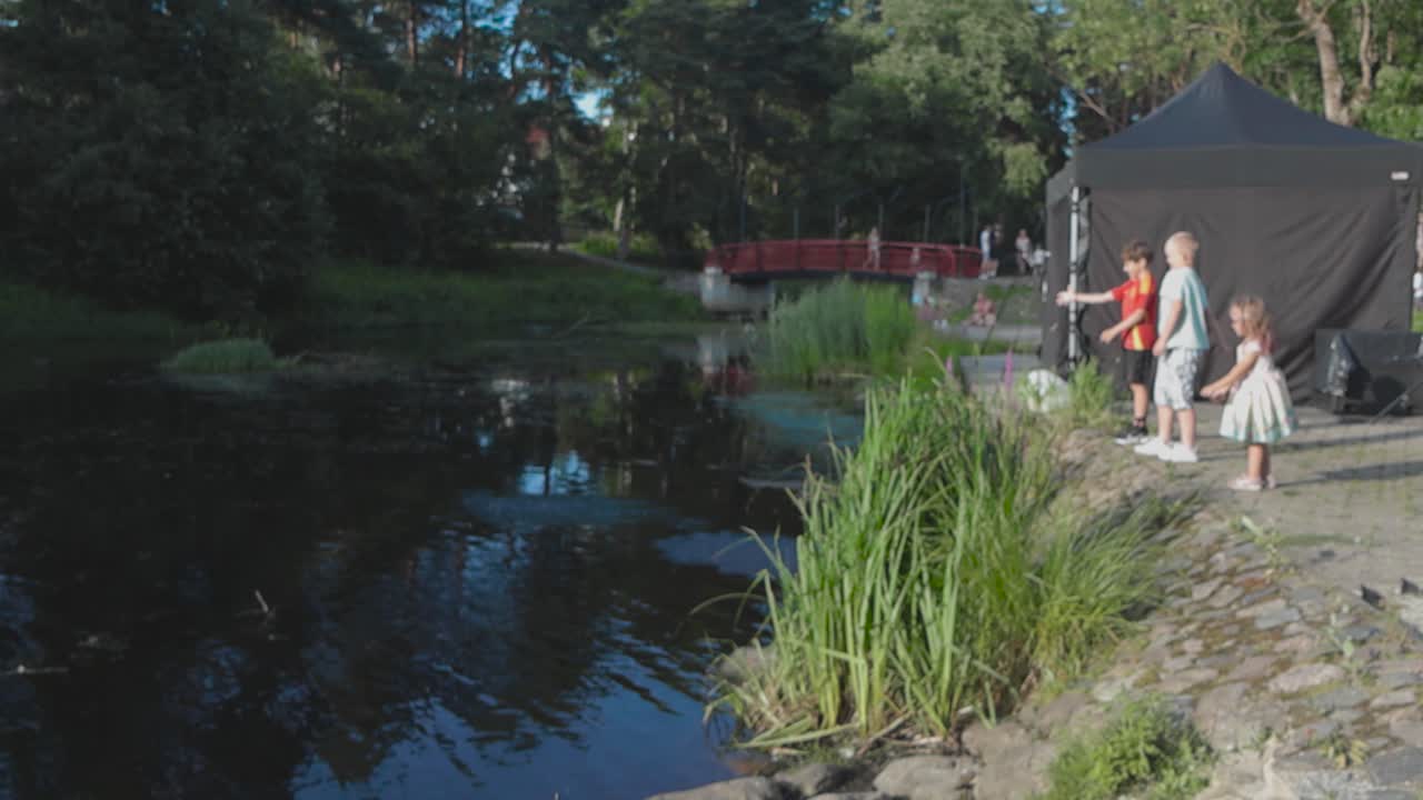 Children by a pond in a park during an outdoor event
