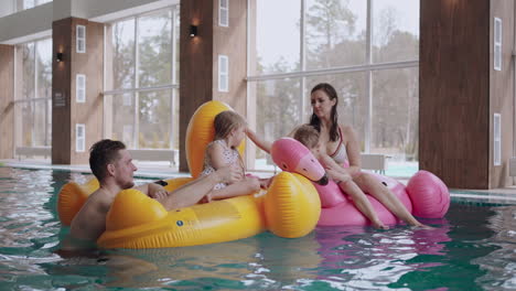 little children with parents are playing in pool and floating on inflatable duck and flamingo indoor pool