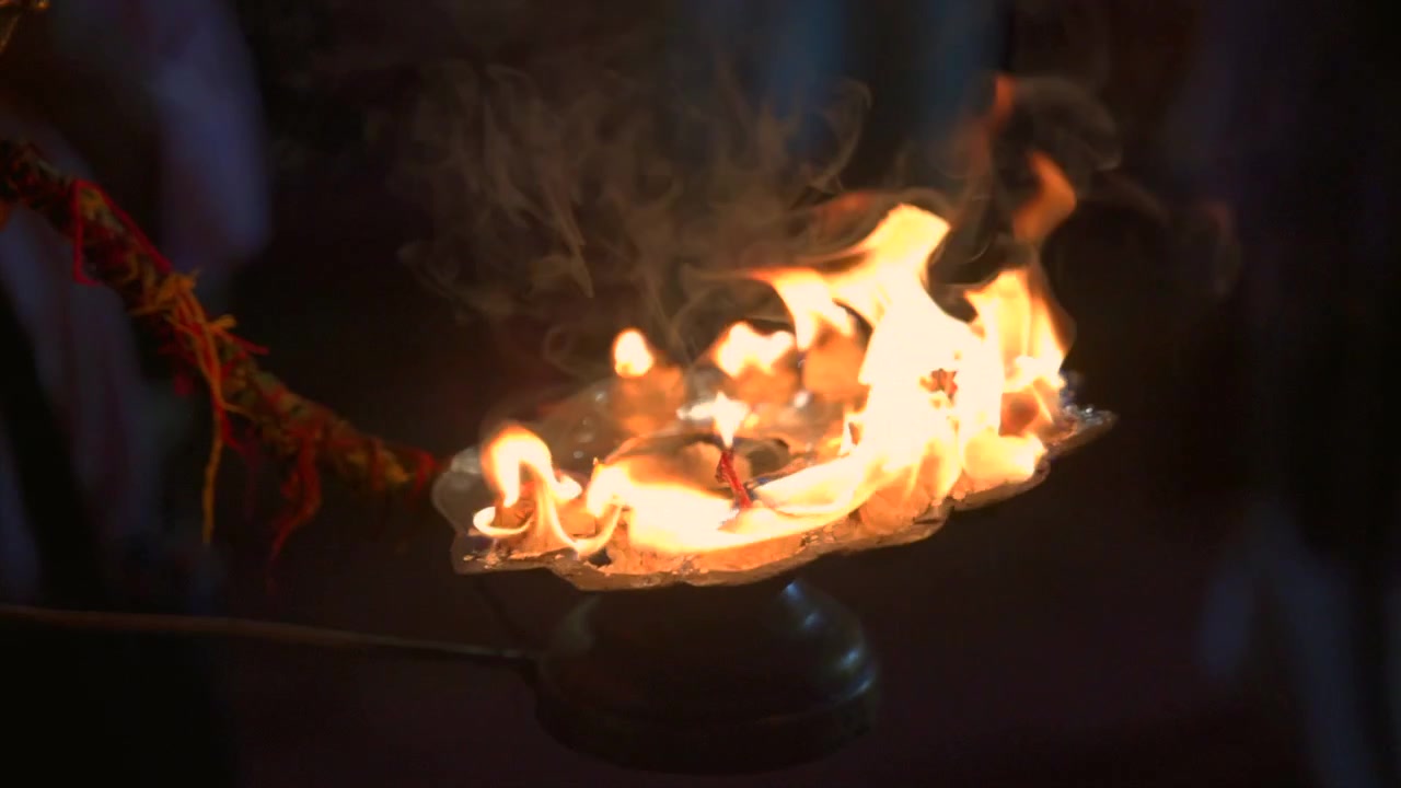Llamas sagradas arden intensamente en una lámpara de latón ornamentada con humo ascendente durante una ceremonia nocturna en cámara lenta, en Vrindavan, India