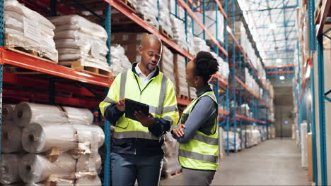 two warehouse workers discuss inventory while looking at a tablet