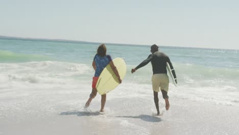 senior african american couple running with surfboard on sunny beach