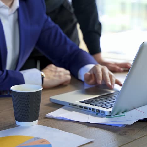 man working on a laptop at desk. laptop on office desk and business partners work in it. male hands on wireless gadget and a plastic cup on table nearby
