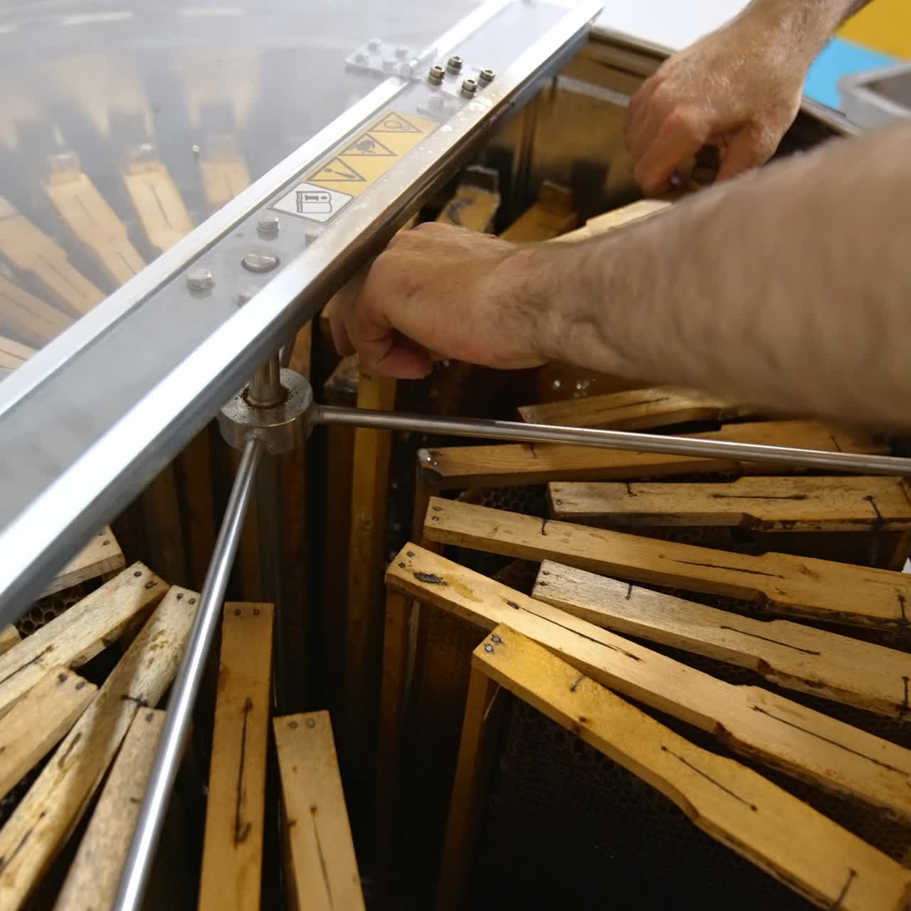 Metal tank with centrifuge inside for extracting honey from honeycombs. Man puts frames side by side into the bin. Close up