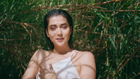 carefree model looking camera in sun beams greenery portrait. happy girl posing