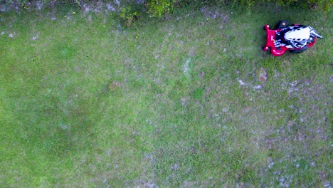 Skeleton-inflatable-dinosaur-costume-mowing-grass-on-zero-turn-mower-viewed-from-overhead-drone-shot