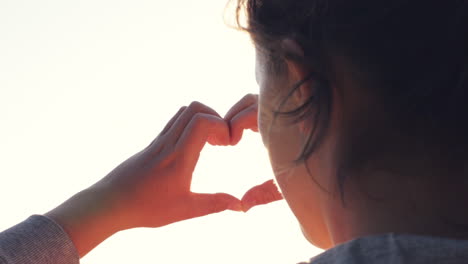 female hands making heart shape gesture holding sun flare