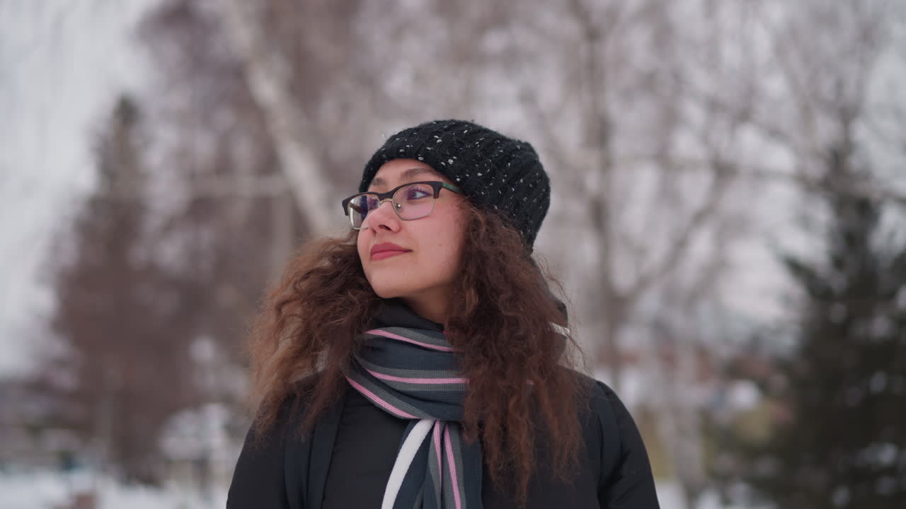 woman looking sideways winter snowy park wearing black coat hat scarf glasses curly hair solitude cold season outdoors frosty atmosphere frozen environment peaceful background overcast sky calm day