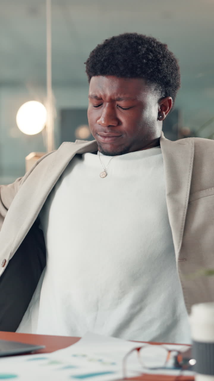 Tired Young Businessman Stretching at His Desk in the Office
