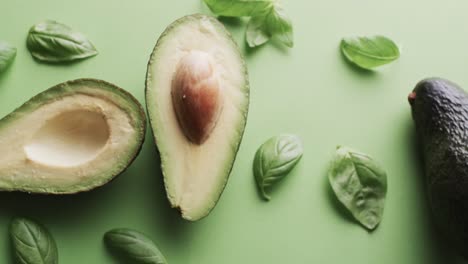 Video-of-sliced-avocado-and-basil-leaves-with-copy-space-over-green-background