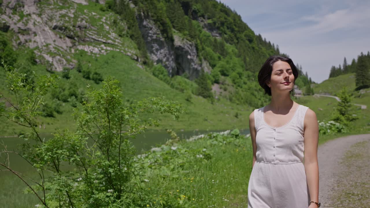 Brunette model walking along river in idyllic Swiss mountains. Sunny summer day in Switzerland. Close up tracking slow motion.