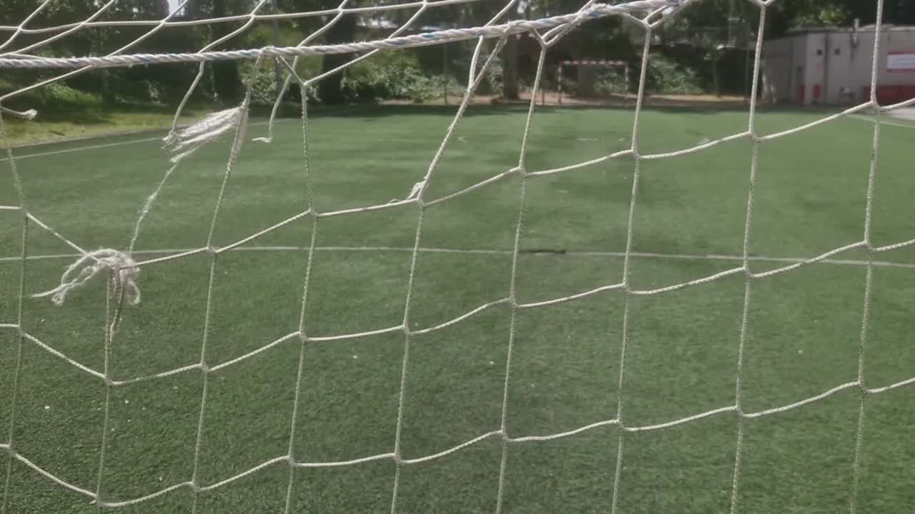 Detaljerad vy som följer ett skadat och sönderrivet fotbollsmålnät på en konstgräsplan.