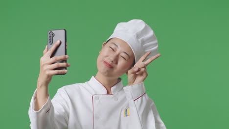 Close Up Of Asian Woman Chef Using Smartphone Taking Picture While Standing In The Green Screen Background Studio