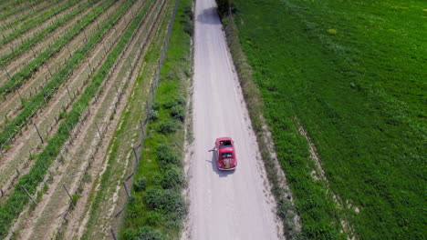 aerial following red car on country road by green farmland in tuscany