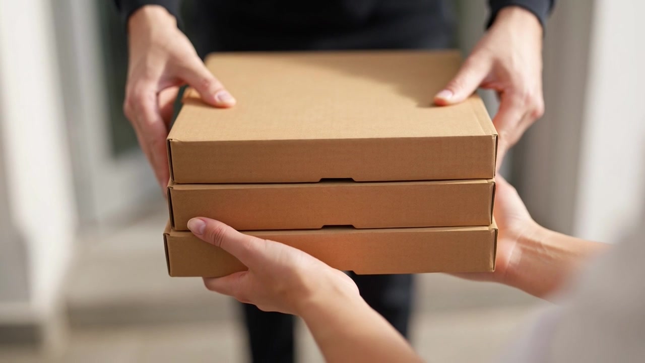 Delivery Person Handing Over Stack of Pizza Boxes to Customer