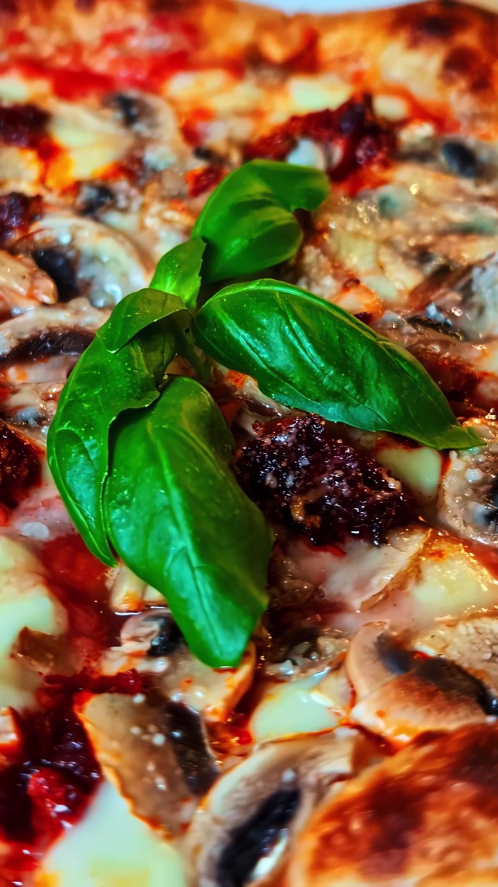 Vista aproximada de uma pizza recém-assada coberta com manjericão, cogumelos e queijo.