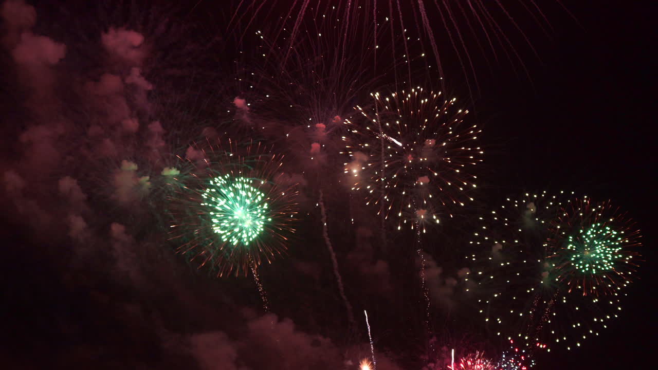 Fireworks fill the night sky with explosions of color to celebrate the new year or independence day. Huge colorful pyrotechnic display with bright flashes and bursting colors sparkle and shimmer