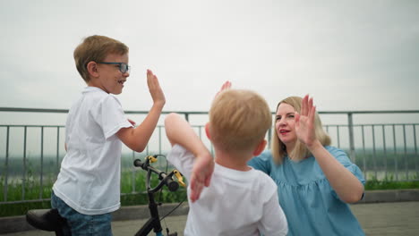 a mother and her two sons joyfully share a high-five outdoors, the kids, full of excitement, happily engage with their mom