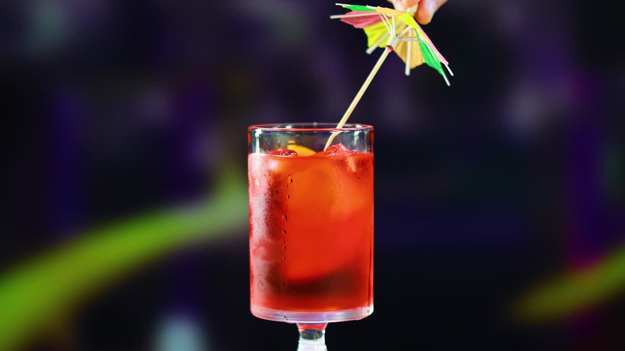 un cóctel de negroni está adornado con un paraguas colorido contra un fondo borroso y vibrante. la iluminación brillante resalta los ricos tonos de la bebida