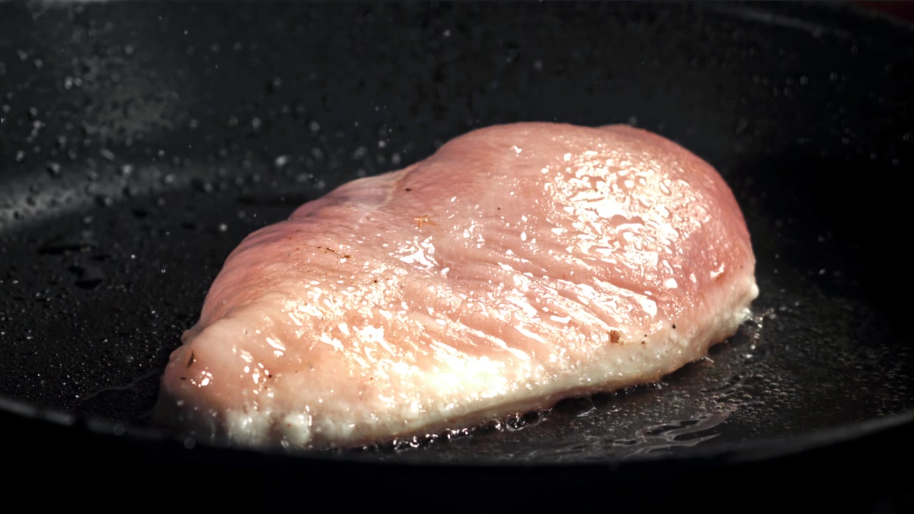 Pollo fresco friéndose en una sartén negra