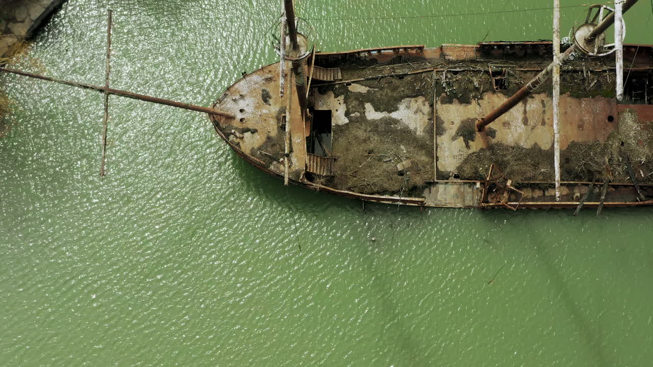 Rusty red shipwreck stuck in shallow green water