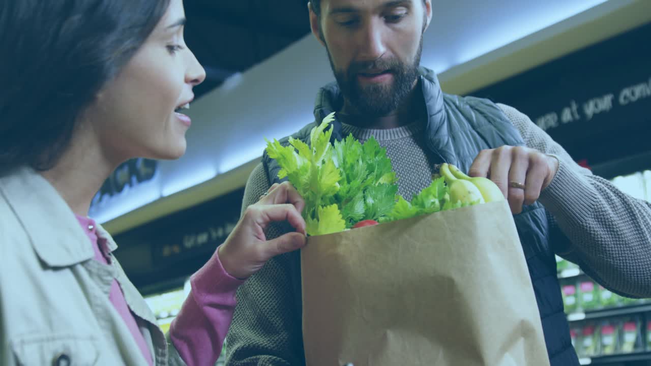 Woman reaching into grocery bag, man arranging produce for packing, map overlay shifting over bag