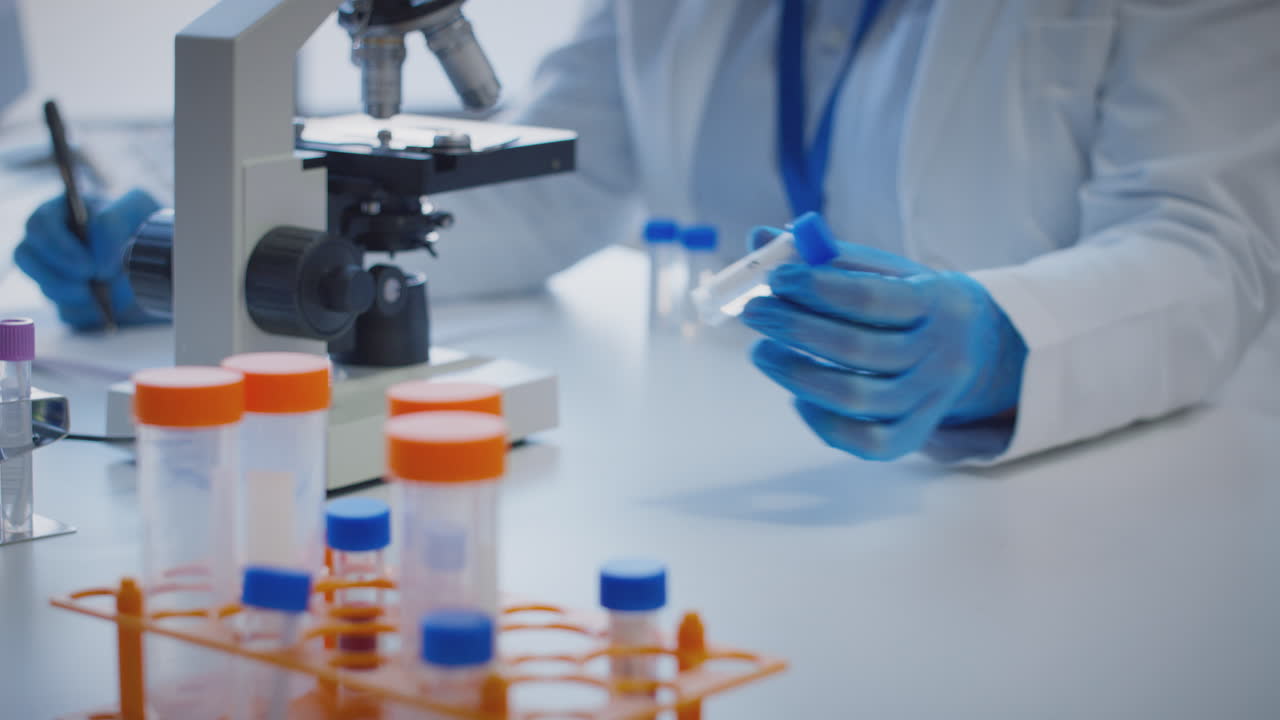 primer plano de un trabajador de laboratorio que lleva a cabo investigaciones utilizando un microscopio con un tubo de ensayo etiquetado xi