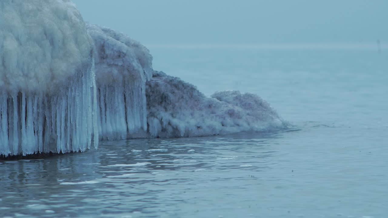 Small waves breaking against the ruins of Karosta Northern Forts fortification on the shore of Baltic sea on a cloudy winter day, covered with ice, snow and icicles, medium closeup shot