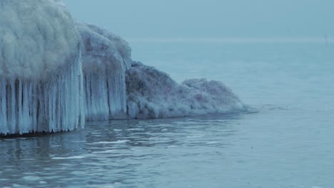 Pequeñas-Olas-Rompiendo-Contra-Las-Ruinas-De-La-Fortificación-De-Los-Fuertes-Del-Norte-De-Karosta-En-La-Orilla-Del-Mar-Báltico-En-Un-Día-Nublado-De-Invierno,-Cubierto-De-Hielo,-Nieve-Y-Carámbanos,-Toma-De-Primer-Plano-Medio