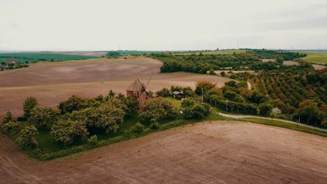 Die-Hölzerne-Windmühle-Steht-Auf-Der-Grünen-Wiese,-Umgeben-Von-Bäumen