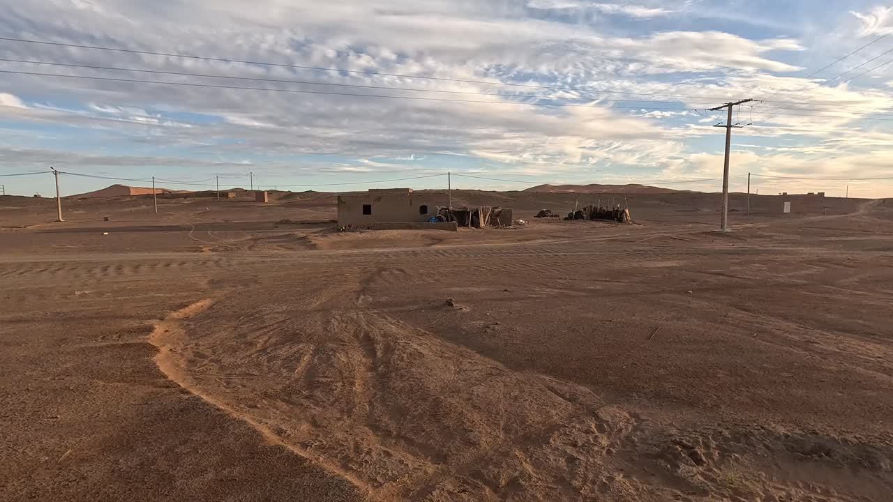 Un insediamento remoto si erge in mezzo al paesaggio arido di Merzouga nel deserto del Sahara, Marocco - Ripresa con drone in orbita.