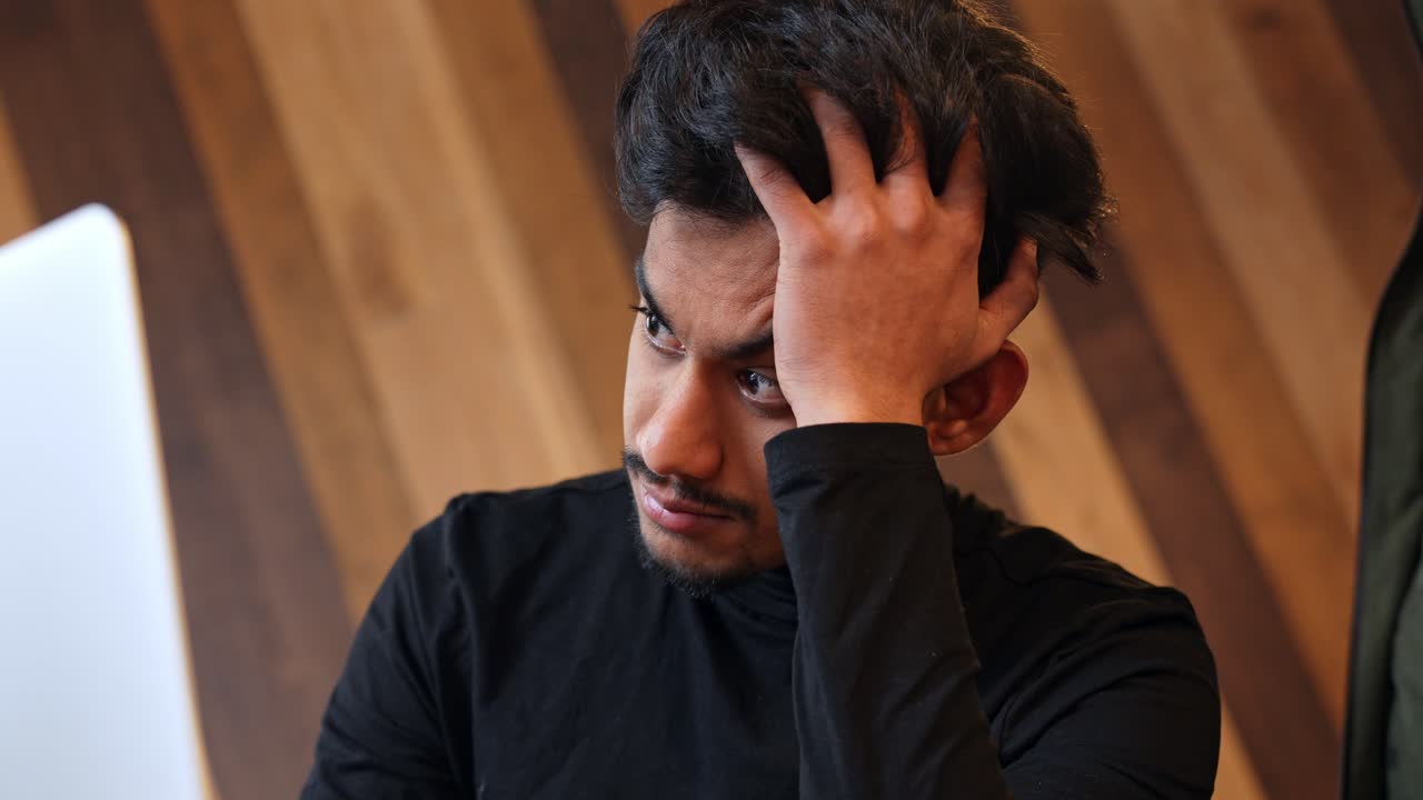 hombre guapo pero cansado de sri lanka sentado cerca de la pantalla de la computadora, vista delantera