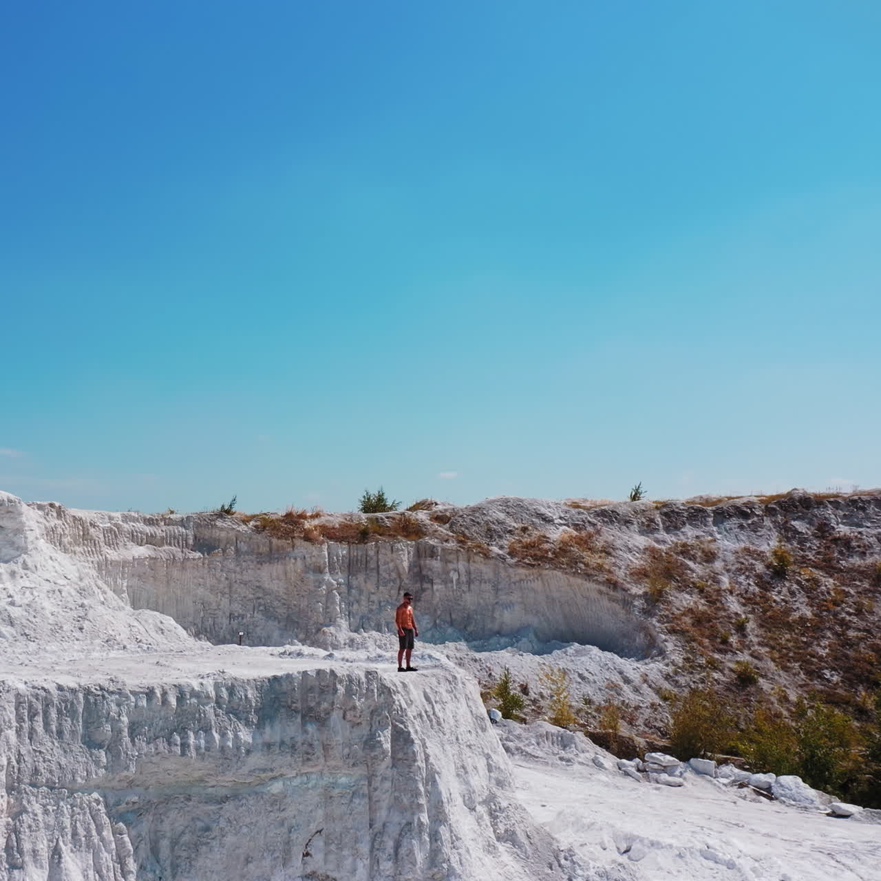 Drone view on a sporty man in canyon. Sportsman in shorts standing on the edge of the white hill in a bright summer day. Aerial view.