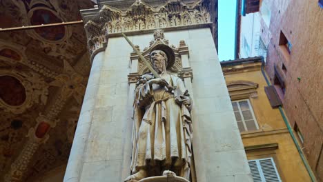 una estatua adorna un pilar de la logia de los comerciantes, loggia della mercanzia ubicada detrás de la plaza del campo, en siena, italia