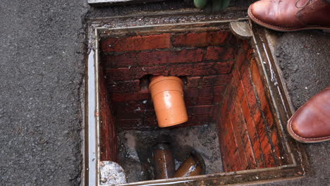 inspecting drain sewer man with gloves on points to problem at open manhole