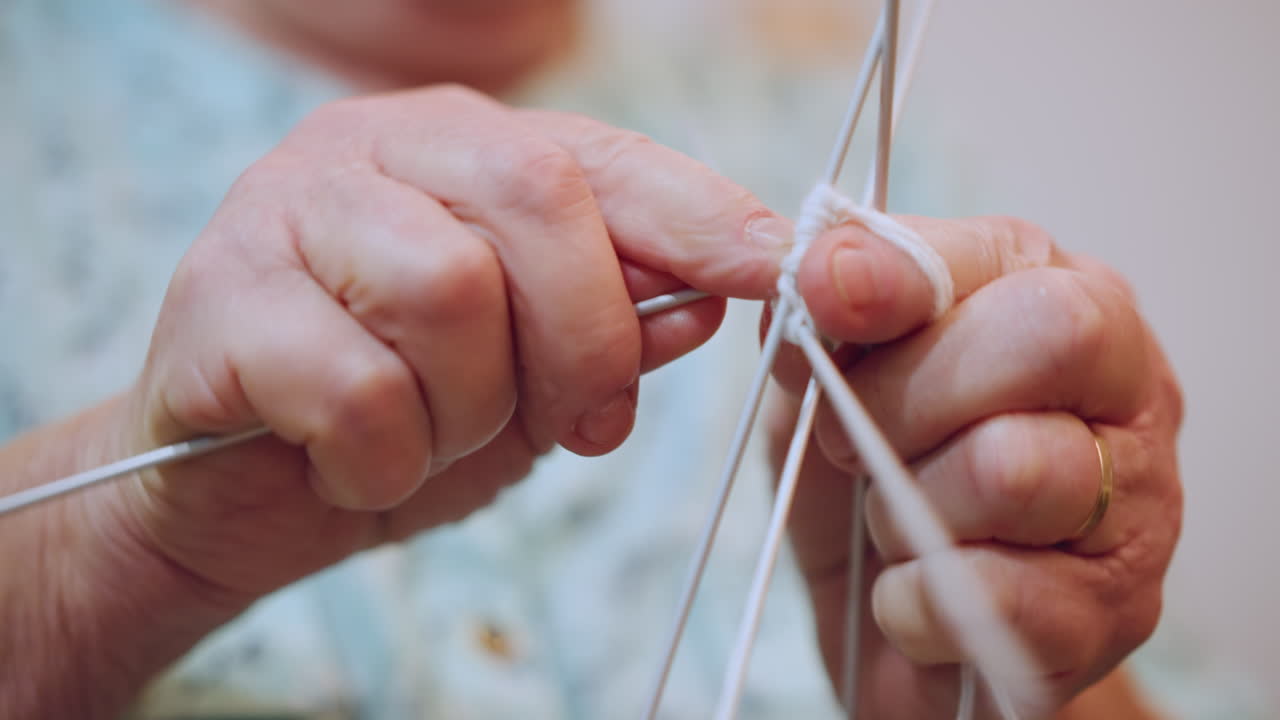 Graceful elderly female delicately crafting stitches with precise movements. Mature Caucasian grandmother carefully manipulating multiple needles to produce intricate knitted patterns